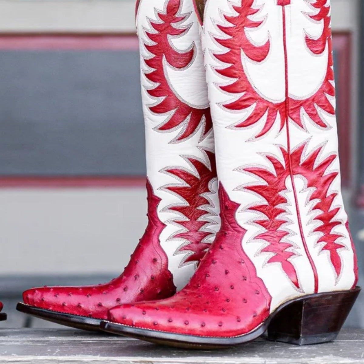 Red and white ostrich leather cowboy boots with intricate western stitching, shown from a close-up angle.