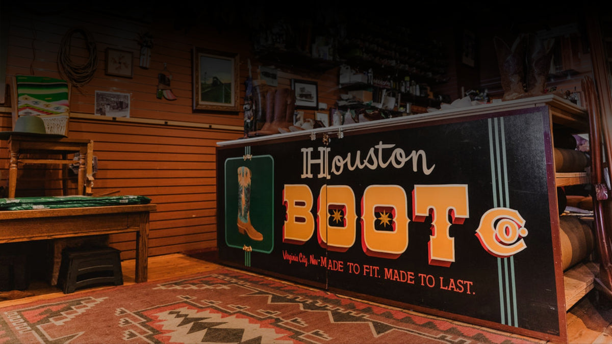 A large counter sign reading 'Houston BOOT Co' with a cowboy boot graphic and western text, displayed in the retail location. The shop interior room has wood-paneled walls and shelves.