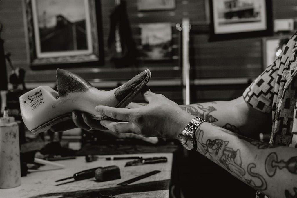 A close-up black and white photo of a Jake holding a shoe form set in a workshop environment.