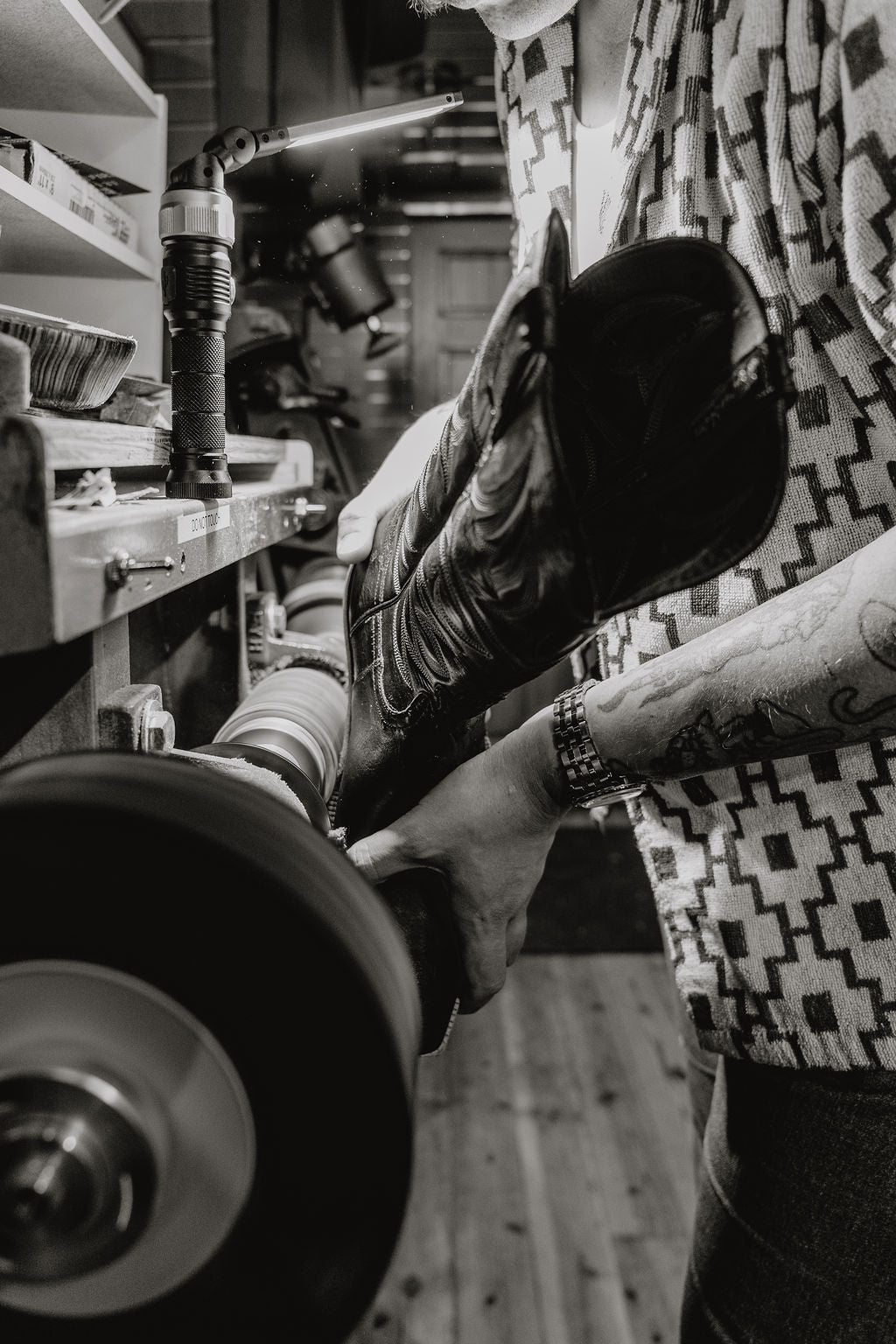 A black and white close-up photo of the maker working on a pair of boots in the workshop.